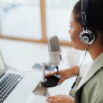 Woman in Teal Blazer Using Black and Silver Headphones in Front of Silver Laptop